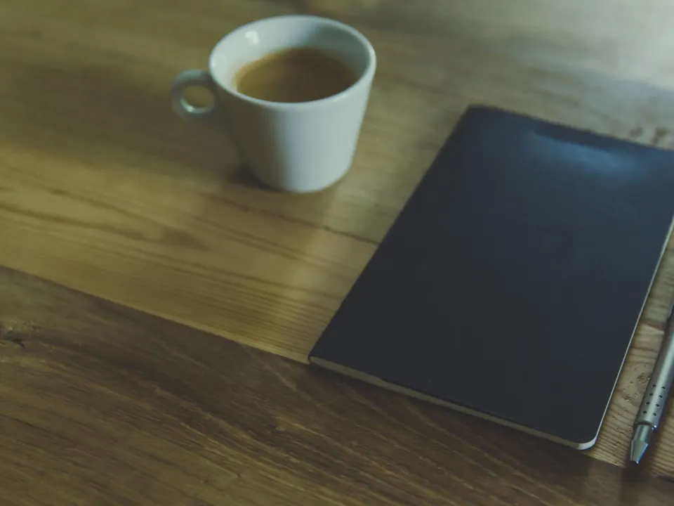 A cup of coffee and a closed notebook on a wooden table