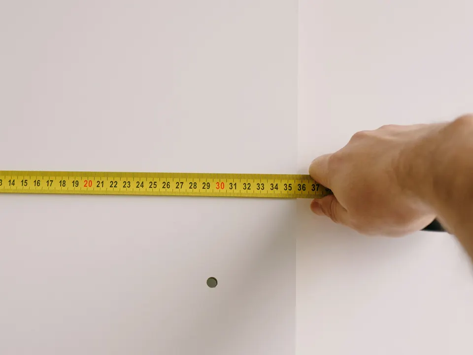 A hand holding a tape measure across a white wall
