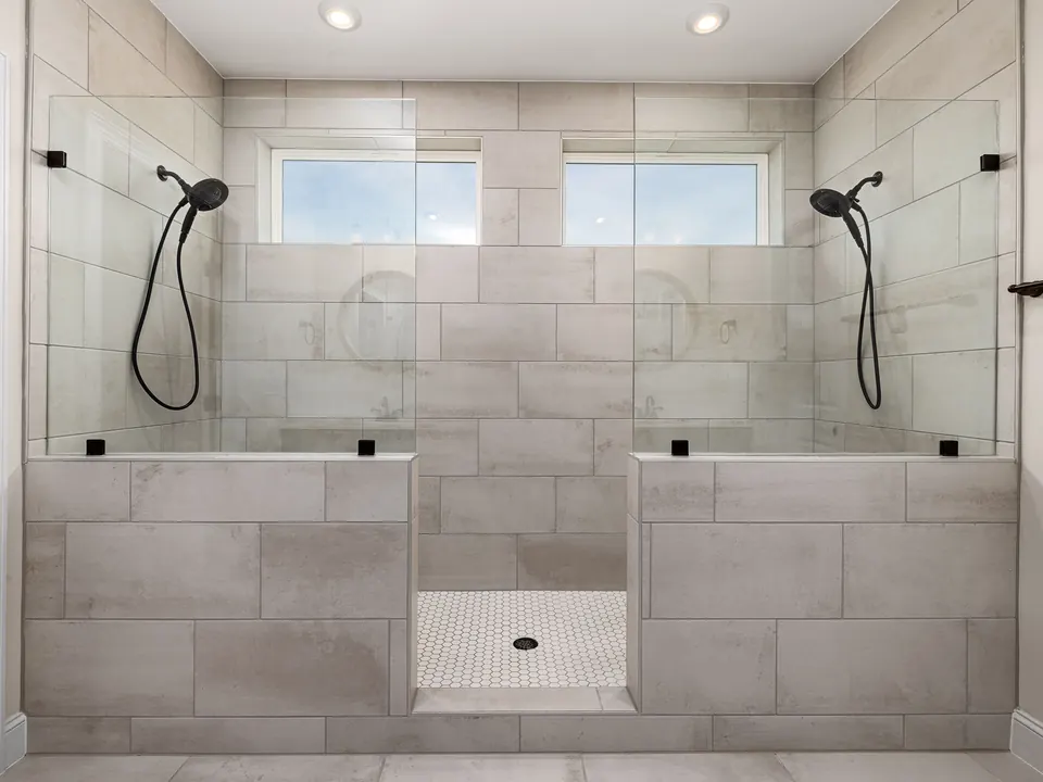 A finished walk-in shower with two shower heads and large grey tiles